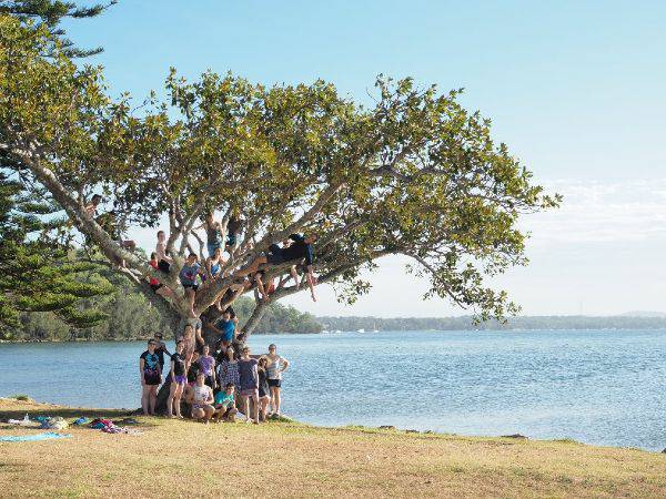 College residents on a retreat at the base of a tree in front of water.
